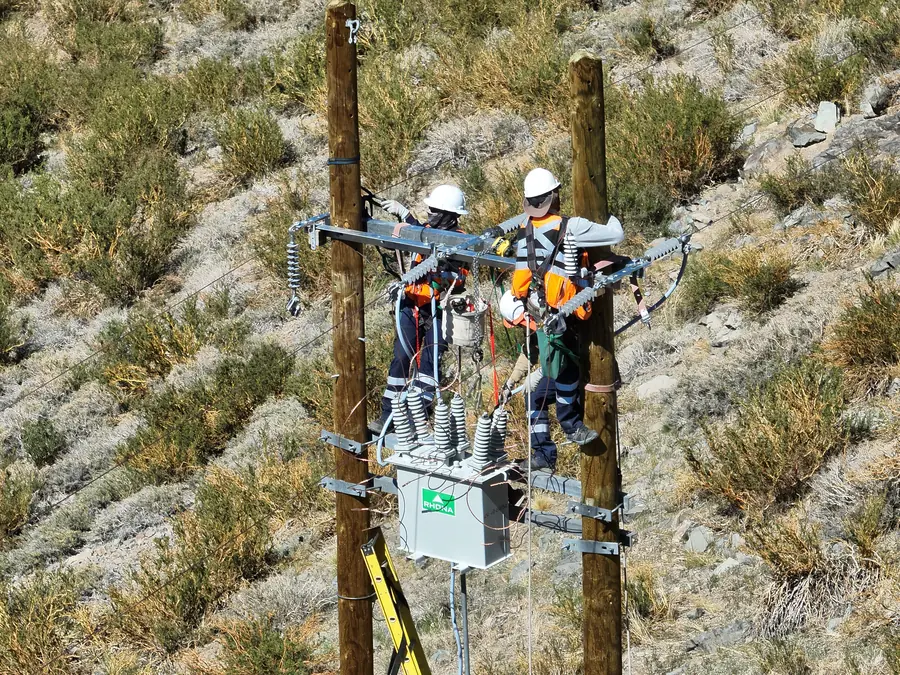 Dos linieros trabajando sobre una estructura portal de media tensión en 23 kV